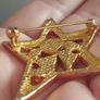A gold star-shaped brooch. Image 4