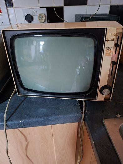 Ideal Prop, Vintage Working Boots Audio TV12 Portable Black and White CRT Television, featuring a cream plastic casing with side control dials and a 12 inch screen. Designed with dual power capabilities supporting standard mains voltage (240V) as well as 