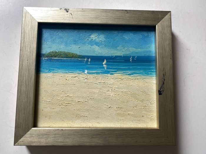 original impasto oil painting on canvas depicts a sunny coastal beach scene with sailboats on the water and a headland in the background
