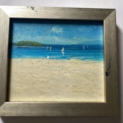 original impasto oil painting on canvas depicts a sunny coastal beach scene with sailboats on the water and a headland in the background