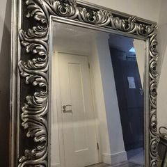 Ornate silver-finished wall mirror with a baroque style carved frame featuring deep acanthus leaf and swirling scroll motifs.
