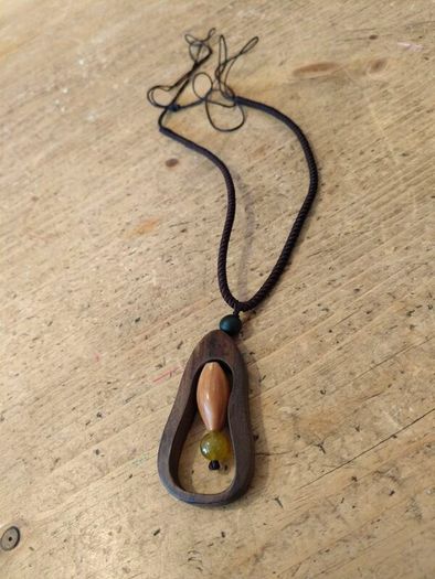 wooden pendant necklace featuring a dark brown wooden frame, a light-colored central bead, and a small dark yellow stone accent on an adjustable braided cord.
