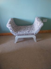 End of bed upolstered seat with curved arms, grey and beige floral pattern.