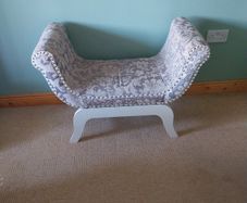 End of bed upolstered seat with curved arms, grey and beige floral pattern.