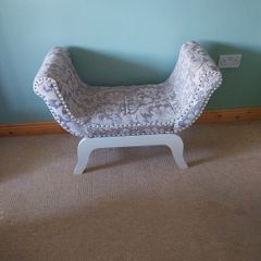 End of bed upolstered seat with curved arms, grey and beige floral pattern.