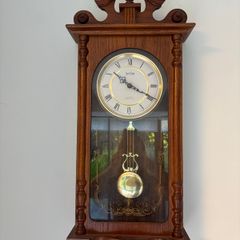 Acctim quartz battery-operated pendulum regulator wall clock housed in a carved wooden case with a dark oak finish.