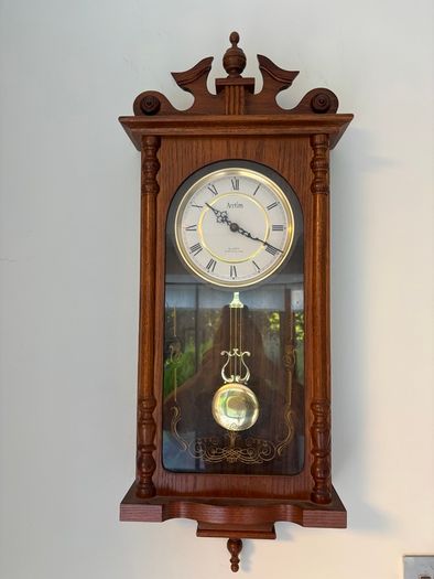 Acctim quartz battery-operated pendulum regulator wall clock housed in a carved wooden case with a dark oak finish.