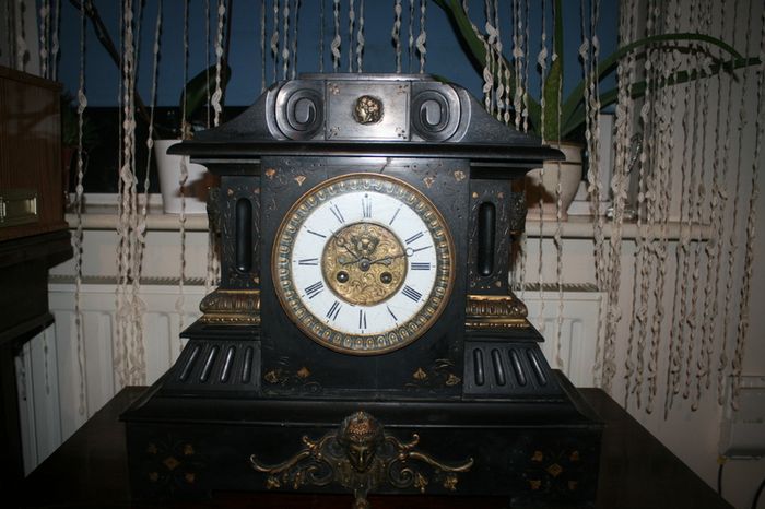 Victorian French Black Slate Mantle Clock (Very large and heavy) with bronze ornamentation Oversized. Open escarpment slate plate Roman numerals. Circa 1890s. Accented with Trojan head. Flanked by two Hellenistic ladies heads on sides. Rose cartouche mask