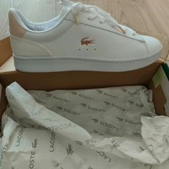 Brand new white Lacoste sneakers with blush pink suede heel detail and signature gold crocodile logo. Classic low-top design with white laces and chunky sole for everyday comfort. Never worn, in perfect condition, and comes with original box. Stylish, cle