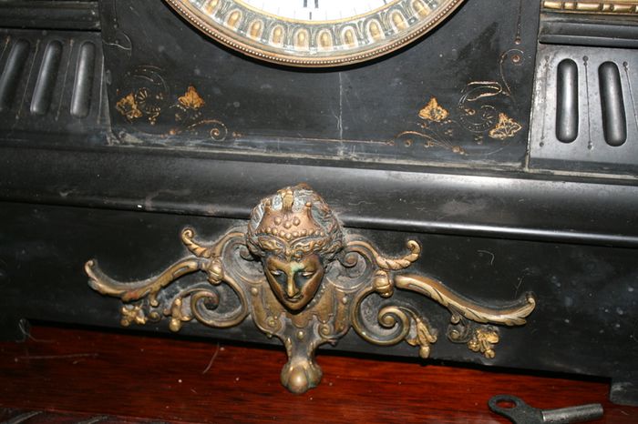 Victorian French Black Slate Mantle Clock (Very large and heavy) with bronze ornamentation Oversized. Open escarpment slate plate Roman numerals. Circa 1890s. Accented with Trojan head. Flanked by two Hellenistic ladies heads on sides. Rose cartouche mask