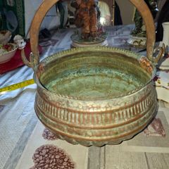 Antique Copper Cauldron features a Rustic Patina, a Swing Handle, and Distinctive Ribbed Detailing around the Rim. It resembles vintage metal pots often used for hearth decoration or as Planters. The piece shows significant oxidation and aging, characteri
