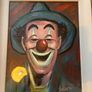 Portrait of a smiling clown wearing a green brimmed hat, red nose, and blue/green face paint around the eyes and mouth. Image 2