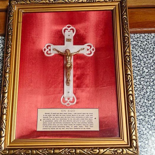 antique framed crucifix featuring a white ornamental cross with a metallic corpus of Jesus Christ mounted over a red  backing inside a gilded wooden frame. Devotional item.