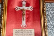 antique framed crucifix featuring a white ornamental cross with a metallic corpus of Jesus Christ mounted over a red  backing inside a gilded wooden frame. Devotional item.