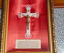 antique framed crucifix featuring a white ornamental cross with a metallic corpus of Jesus Christ mounted over a red  backing inside a gilded wooden frame. Devotional item.