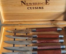 A Newbridge Cuisine set of six steak knives with serrated blades and wooden handles.