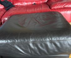 This dark brown leather footstool features a soft, square silhouette with visible top-stitching and short wooden block feet.