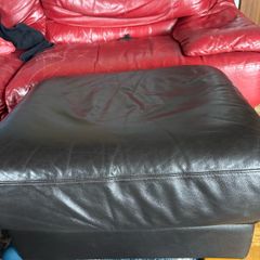 This dark brown leather footstool features a soft, square silhouette with visible top-stitching and short wooden block feet.