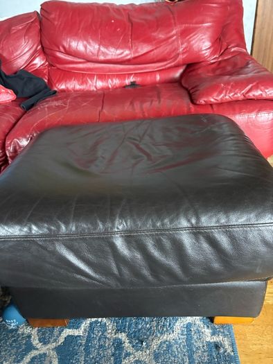 This dark brown leather footstool features a soft, square silhouette with visible top-stitching and short wooden block feet.