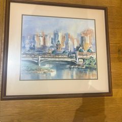 The framed watercolor painting appears to depict an impressionistic cityscape featuring a historic stone bridge over a river, similar in style and subject to watercolor prints of Princes Bridge in Melbourne or the Melbourne Skyline with Yarra River