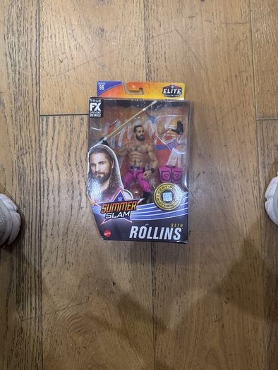 The item shown is the WWE Elite Collection Series 86 SummerSlam Seth Rollins action figure by Mattel, featuring his pink and black ring gear, TrueFX facial detailing, and themed accessories.