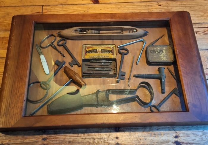 vintage shadow box containing a mix of antique tools, keys, and a loom.