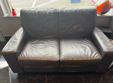 pre-owned black leather two-seater sofa with plump back cushions and wide arms.
