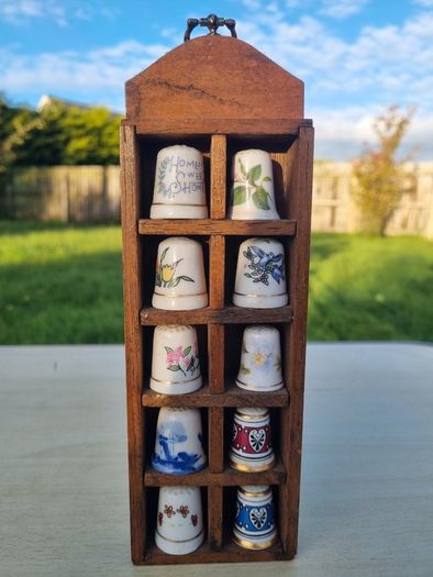 Collectible porcelain thimbles in a wall-mounted wooden display case