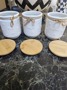 white ceramic tea, coffee, and sugar storage canisters accented with embossed daisy patterns and rustic twine bows.