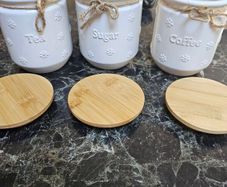 white ceramic tea, coffee, and sugar storage canisters accented with embossed daisy patterns and rustic twine bows.