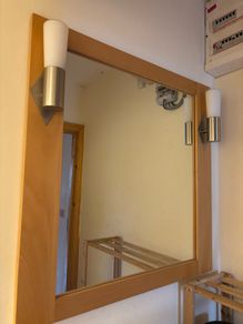 This pine-framed mirror includes two attached wall sconces for lighting.