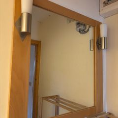 This pine-framed mirror includes two attached wall sconces for lighting.