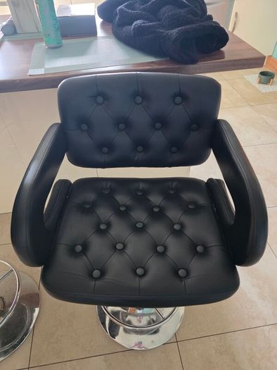 2 black faux leather bar stools with padded seats, armrests and chrome bases.