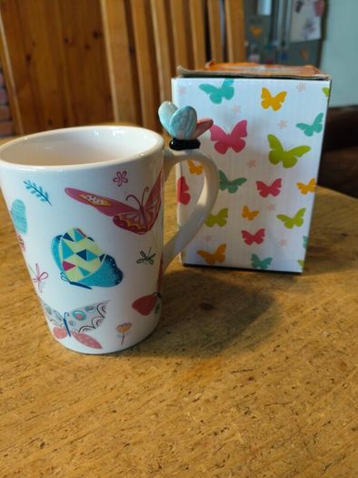 Butterfly Shaped Handle Ceramic Mug, decorated with various colorful butterfly graphics. 3D ceramic butterfly molded directly onto the handle. New in Box.