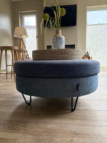 Large Round Blue Ottoman / Footstool with Storage  Stylish round ottoman with a dark denim-blue cushioned top, textured lighter blue base and black metal legs.  The top lifts off to reveal a handy storage space. Perfect as a footstool or styled with a tra