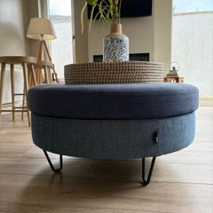 Large Round Blue Ottoman / Footstool with Storage  Stylish round ottoman with a dark denim-blue cushioned top, textured lighter blue base and black metal legs.  The top lifts off to reveal a handy storage space. Perfect as a footstool or styled with a tra