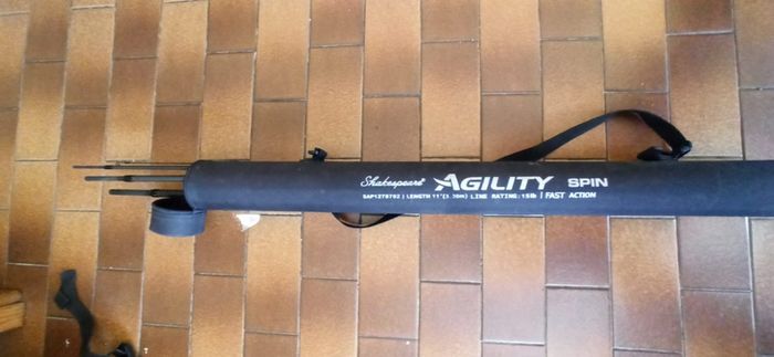 Shakespeare Agility Spin fishing rod. 11 feet (3.30 meters) in length. The item includes a black carrying tube with a strap for transport.