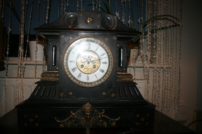 Victorian French Black Slate Mantle Clock (Very large and heavy) with bronze ornamentation Oversized. Open escarpment slate plate Roman numerals. Circa 1890s. Accented with Trojan head. Flanked by two Hellenistic ladies heads on sides. Rose cartouche mask