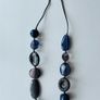A long, multi-strand fashion necklace featuring a variety of chunky blue and translucent resin and glass beads strung on a dark cord Image 2