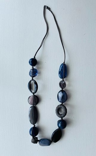 A long, multi-strand fashion necklace featuring a variety of chunky blue and translucent resin and glass beads strung on a dark cord