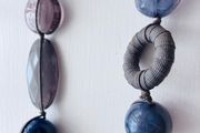 A long, multi-strand fashion necklace featuring a variety of chunky blue and translucent resin and glass beads strung on a dark cord