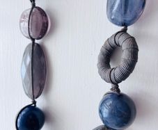 A long, multi-strand fashion necklace featuring a variety of chunky blue and translucent resin and glass beads strung on a dark cord