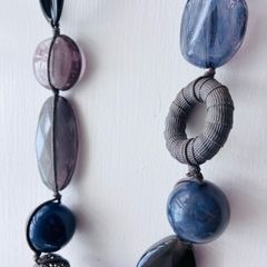 A long, multi-strand fashion necklace featuring a variety of chunky blue and translucent resin and glass beads strung on a dark cord