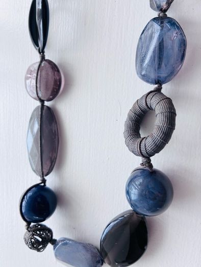 A long, multi-strand fashion necklace featuring a variety of chunky blue and translucent resin and glass beads strung on a dark cord
