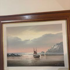 This artwork is a coastal oil painting featuring a traditional single-masted sailing boat stranded or anchored on a calm shoreline, signed by contemporary marine artist David James