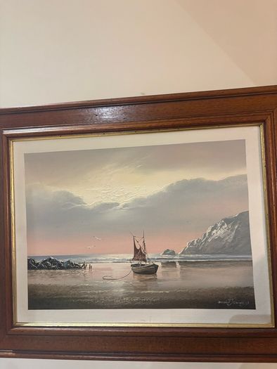 This artwork is a coastal oil painting featuring a traditional single-masted sailing boat stranded or anchored on a calm shoreline, signed by contemporary marine artist David James