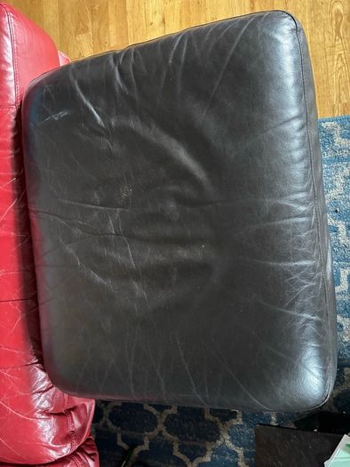 This dark brown leather footstool features a soft, square silhouette with visible top-stitching and short wooden block feet.