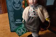 Collectors porcelain Irish doll from the "Collectors Dolls" range by Shannon Distributors. It is specifically marketed as a doll featuring traditional Irish dresses, as indicated by the tag it's holding. It is new in box.