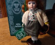 Collectors porcelain Irish doll from the "Collectors Dolls" range by Shannon Distributors. It is specifically marketed as a doll featuring traditional Irish dresses, as indicated by the tag it's holding. It is new in box.