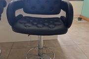 2 black faux leather bar stools with padded seats, armrests and chrome bases.
